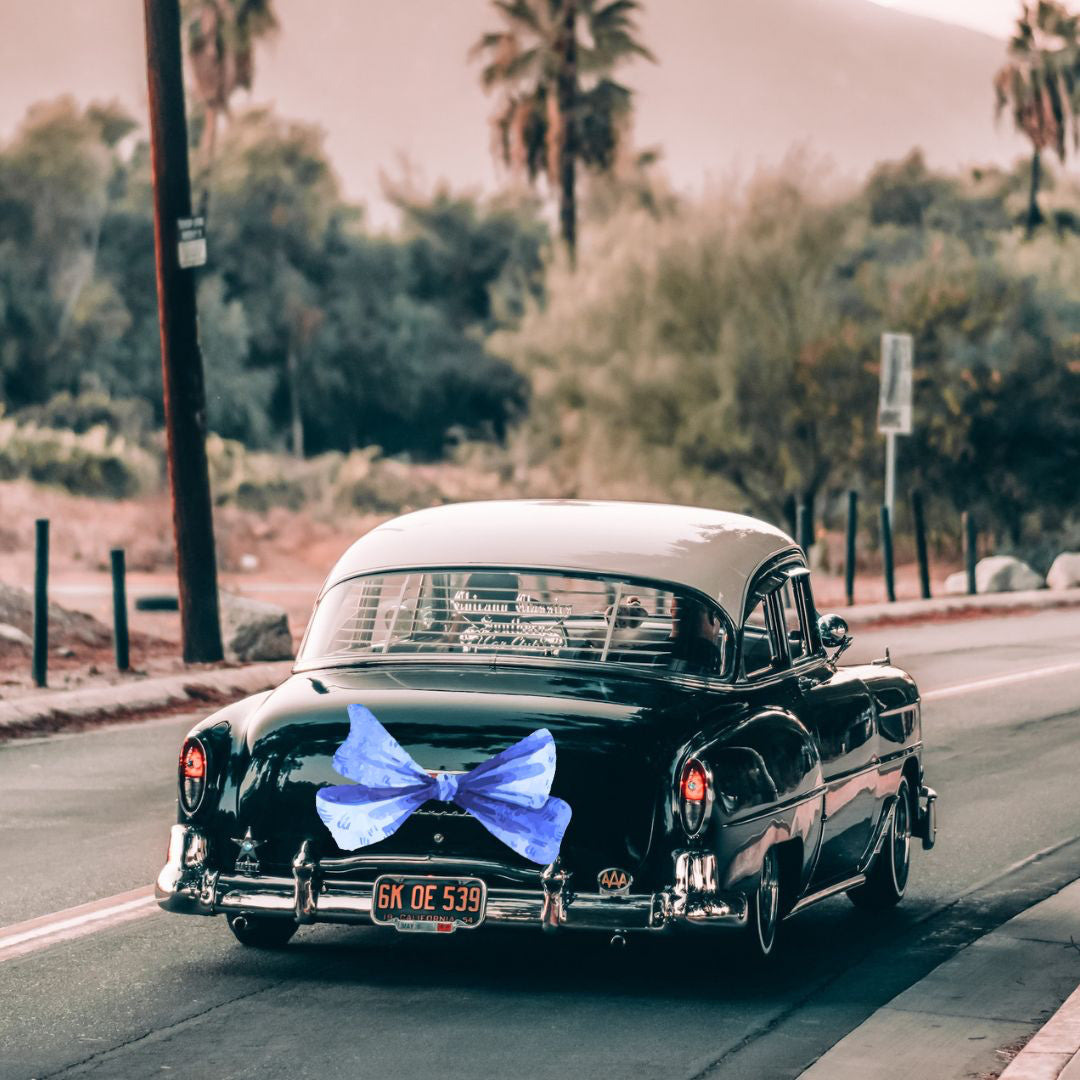 a black vintage car traveling on a road with palm trees in the back