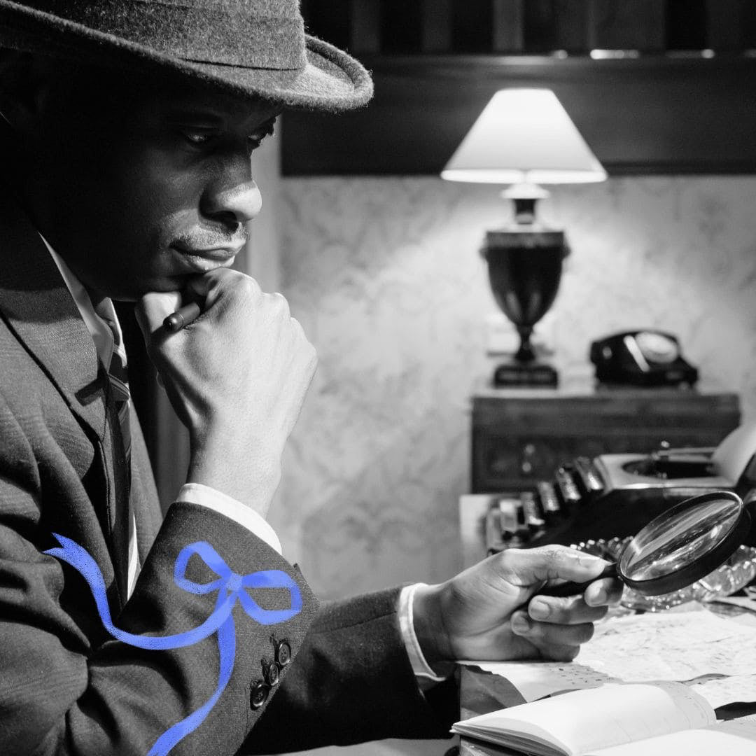 Man in a suit and hat holding a magnifying glass, sitting at a desk with a lamp and phone in the background.